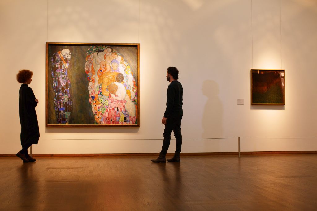 Two people in front of pictures of the Klimt collection at the Leopold Museum in Vienna